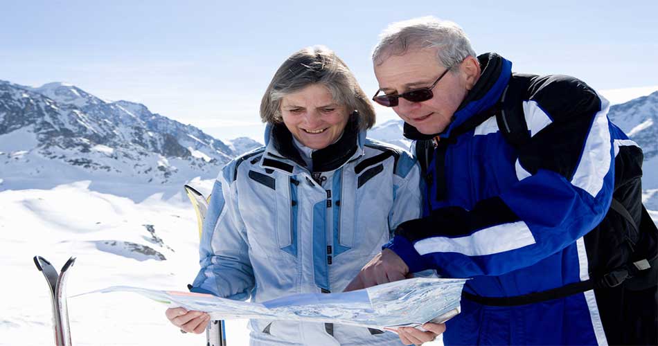 Retiree skiers looking at map, at ski slope.