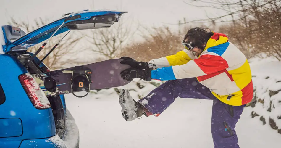 Man shoving snowboard in car.