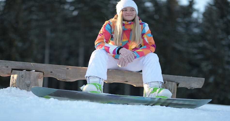 Girl sitting on bench with snowboard.