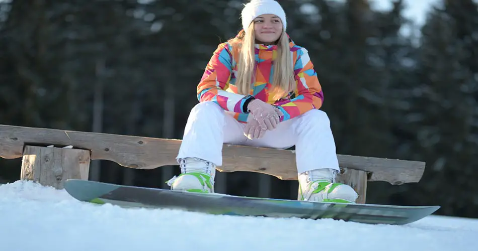 Snowboarder girl sitting with snowboard leash.