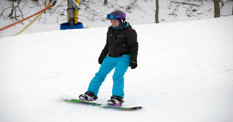 Girl showing how to stop on snowboard.