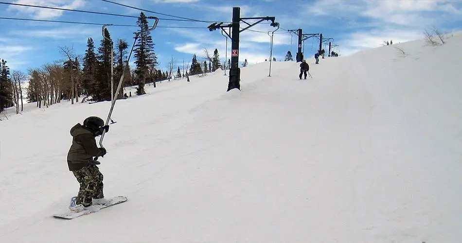 Snowboarder using poma lift at ski resort.