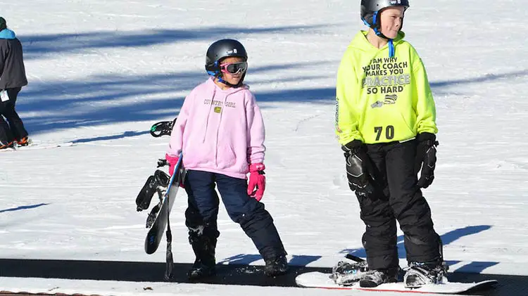 Two kids starting out on snowboards in lessons.